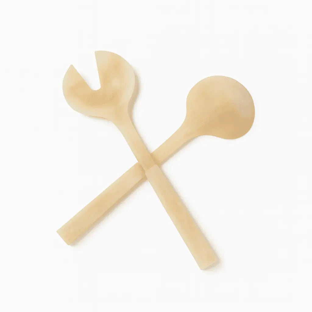 Crossed gold glitter resin salad servers with round bowl and fork ends on white background.