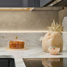 Cream-colored resin cookie jar with lid on marble countertop in modern kitchen, featuring decorative finial and clean minimalist design
