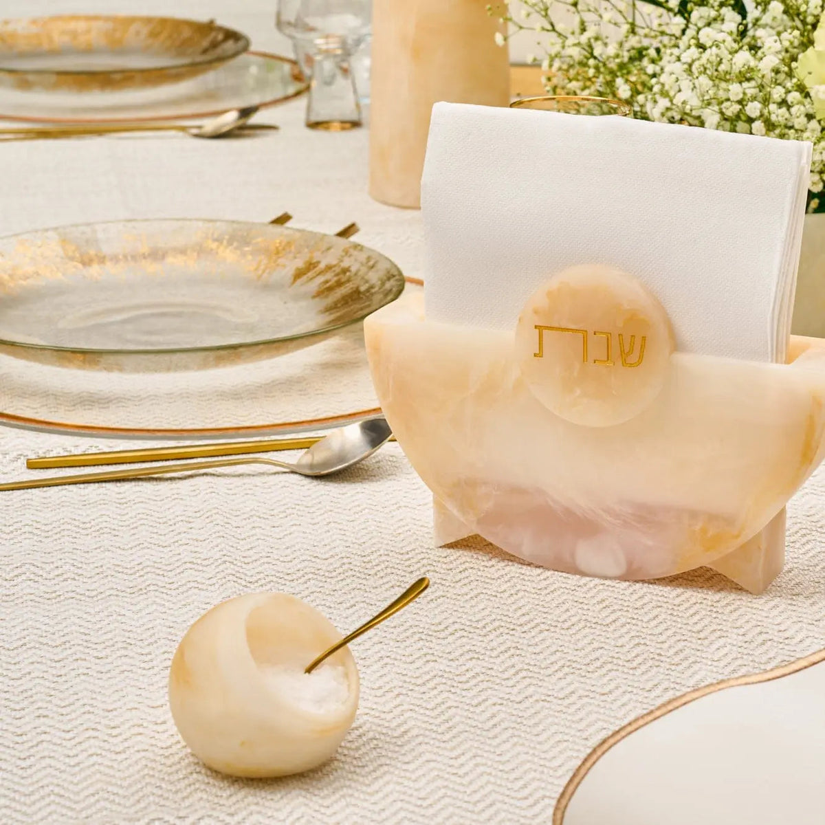 Translucent amber resin salt cellar with matching spoon displayed on elegant table setting with gold accents and place card.