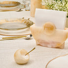 Translucent amber resin salt cellar with matching spoon displayed on elegant table setting with gold accents and place card.