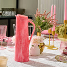 Blush pink faux floral vase with gold accents displayed on a styled table with greenery and candles, part of Waterdale Collection.