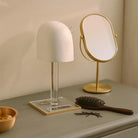 Classic Lucite wig head display stand in white with gold-trimmed mirror and styling accessories on marble surface.