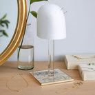 French Toile Lucite wig head with white dome and clear acrylic stand, displayed on desk with mirror and accessories.