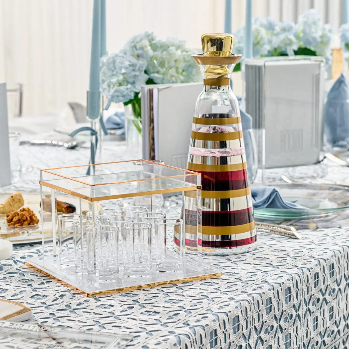 Metallic mixed finish wine decanter with gold and black striped design displayed on white patterned table with glasses and tabletop accessories.