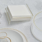 Waterdale Collection raised inspired napkin holder in white with gold metal accent trim, displayed on white tabletop with place settings