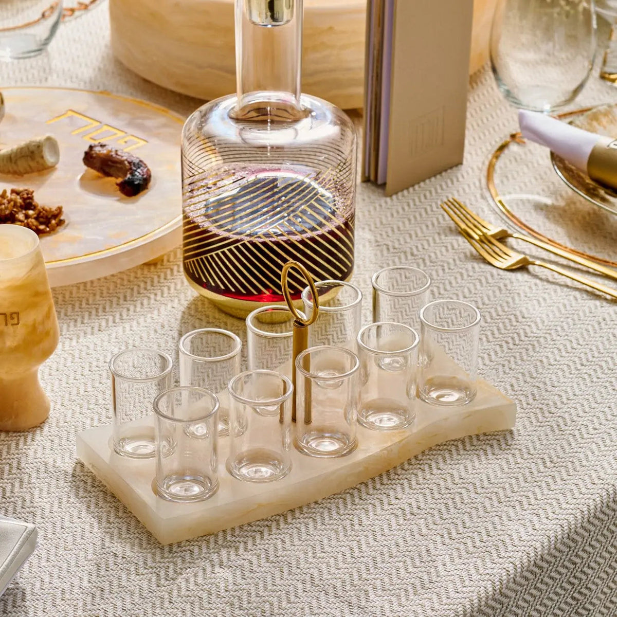 Cream resin liquor set with curved decanter and six matching glasses arranged on a wooden base, styled on a dining table.