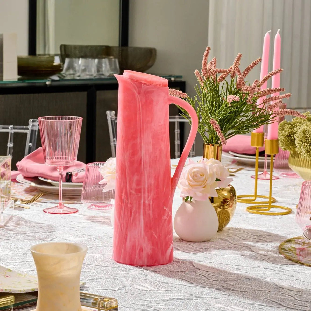 Coral pink resin pitcher with textured surface displayed on a marble table setting with glassware and floral centerpiece.