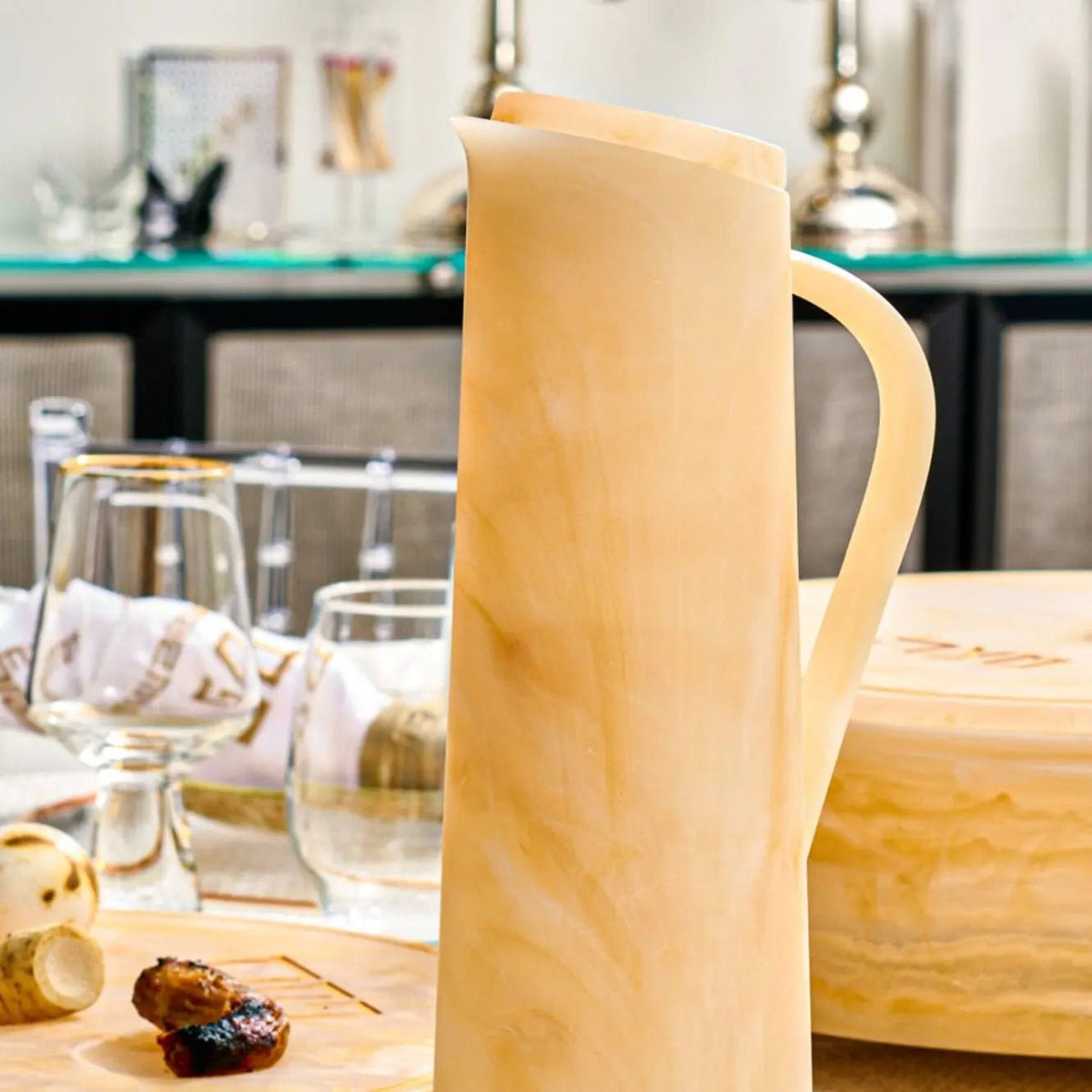 Cream-colored resin pitcher with handle displayed on kitchen counter next to glassware, from Waterdale Collection