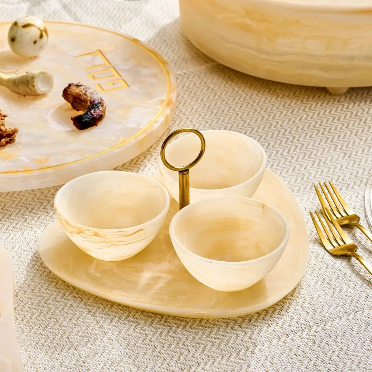 Cream resin round dip bowl set with three small bowls on wooden serving tray, displayed with gold utensils and decorative items.