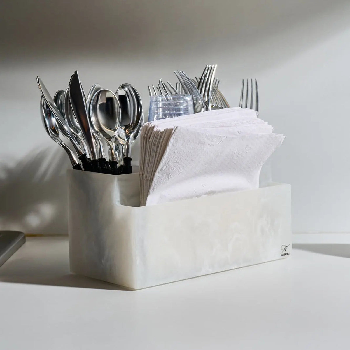 White resin silverware caddy holding various utensils and napkins, modern tabletop organizer for kitchen or dining.