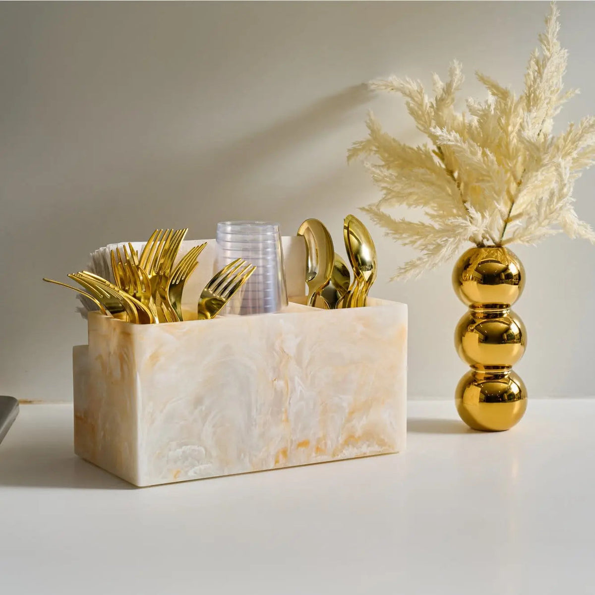 Faux pampas grass in gold vase next to marble cube with gold decorative accents on white surface