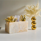 Faux pampas grass in gold vase next to marble cube with gold decorative accents on white surface
