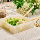 Gold glitter resin square salad bowl filled with green salad at a table setting with wine glasses and white flowers.
