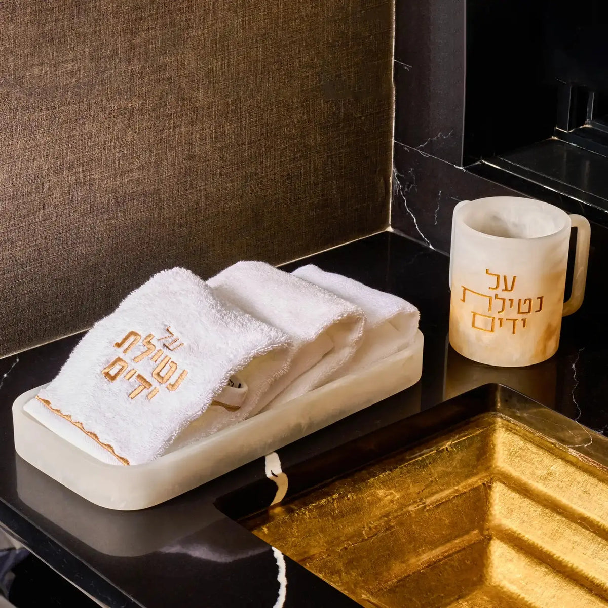 Cream resin towel tray with gold accents holding folded white towels, displayed on a bathroom vanity next to a gold candle holder