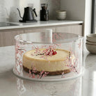 Clear Round Cherry Blossom Cake Dome with hand-painted floral design, displayed on kitchen counter with layered cake inside
