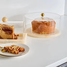 Round clear resin cake dome with gold accent displaying fresh baked cake, serveware for entertaining and holiday tables.