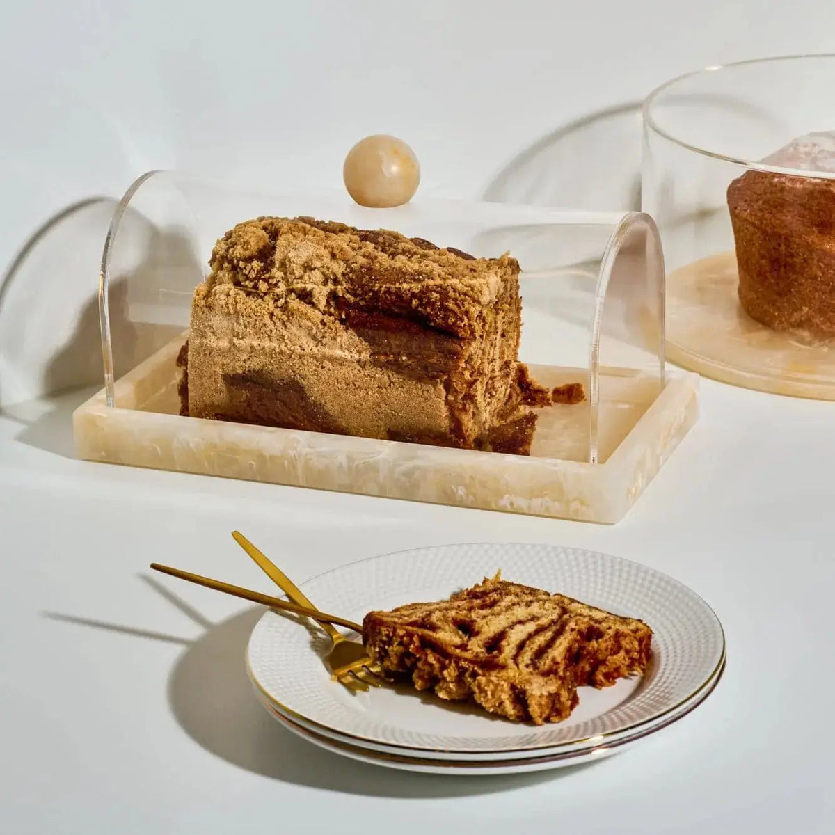 Small rectangular resin cake dome displaying sliced layered cake, shown with a plated pastry on white surface for elegant tabletop serving.
