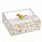 Square floral bird napkin holder with gold leaf design, clear acrylic sides, and decorative gold bird finial on white napkin base.