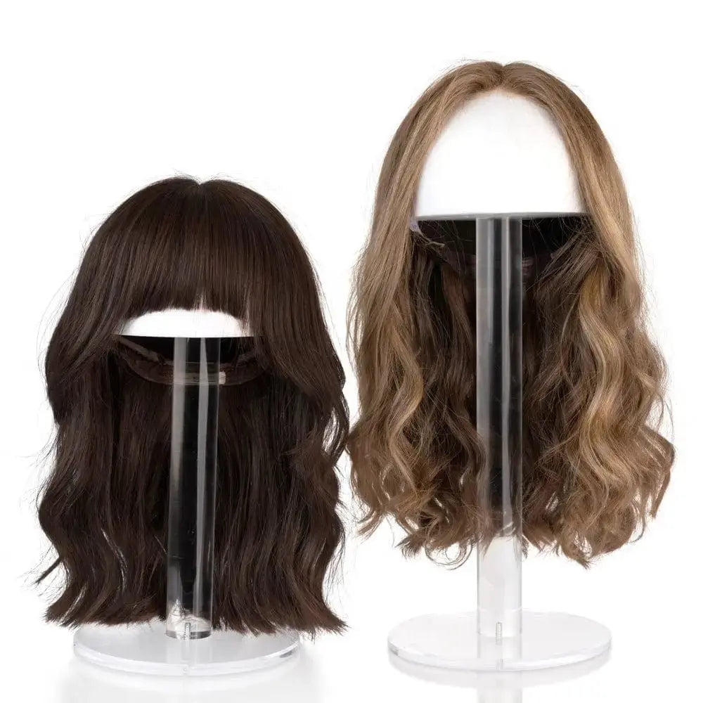 Clear lucite wig head display stand with two wigs: a short dark brown bob and a longer wavy caramel-toned wig, showing wig styling options.
